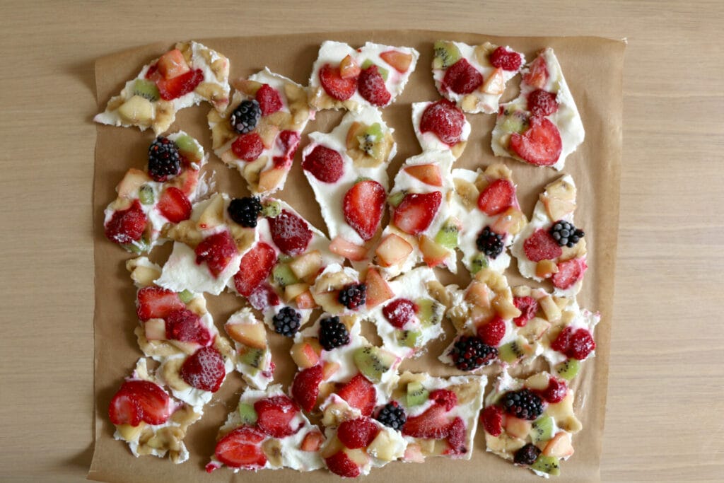 Frozen yogurt bark with various fruit strawberry, banana, kiwi, raspberry, blackberry on parchment paper. Healthy, gluten-free snack.Top view.