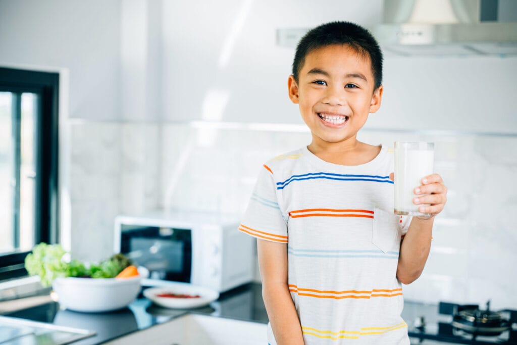 Portrait of cute Asian little boy in kitchen holding milk.
